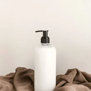 White pump bottle with a black pump on a warm beige surface, beside folded brown cloth