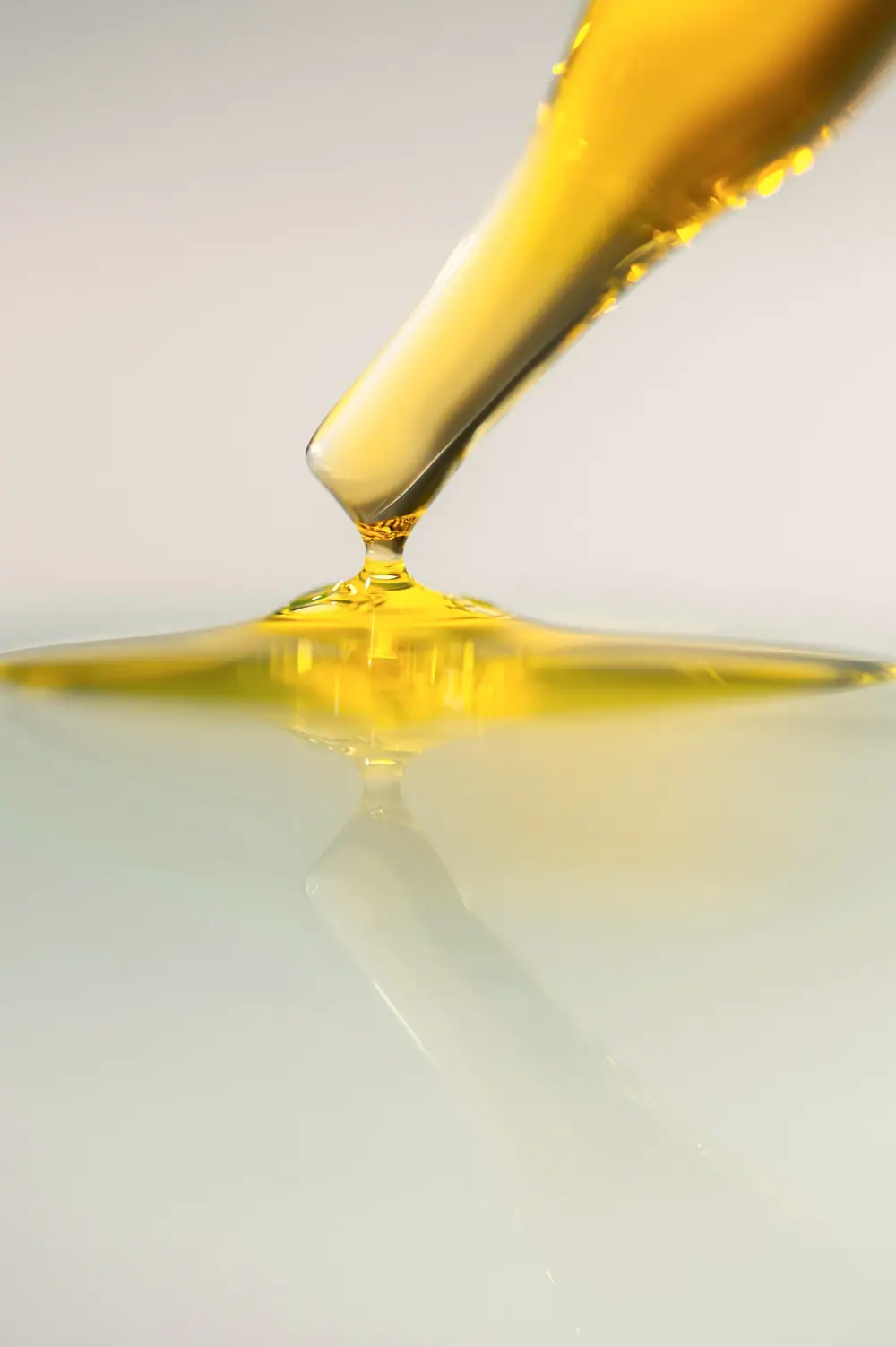 A glass dropper releasing a golden drop of serum onto a pale surface